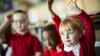 Primary school children raising their hands in a classroom